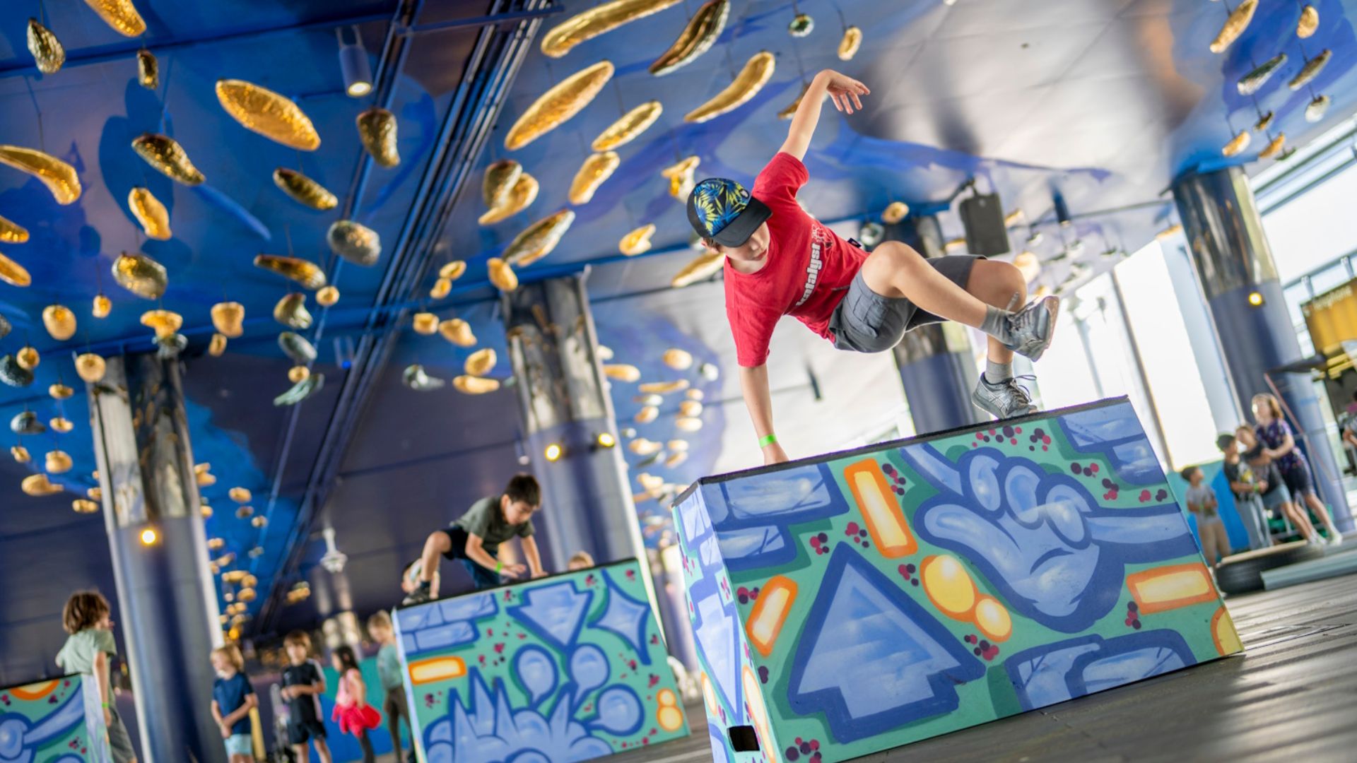 A young parkour student jumps a wall in a red top